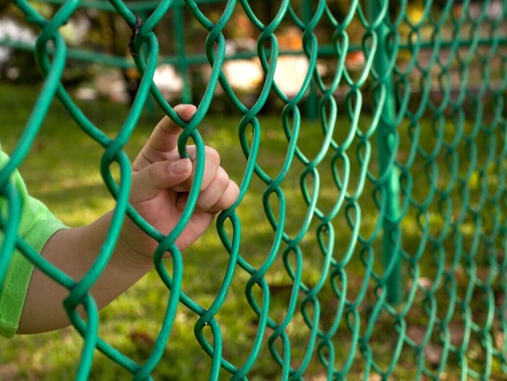 Green chain link fence with vinyl coating and child behind it